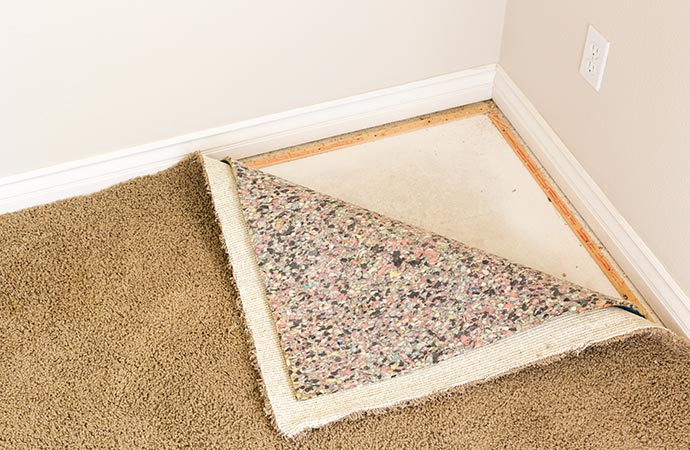 Close-up of carpet tack strips installed along the edge of a room's baseboard.